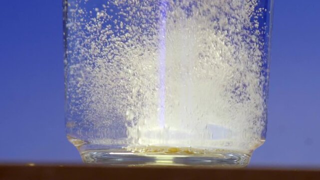Effervescent tablet dissolving in a glass of water. Macro close-up