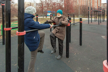 Woman exerciser doing exercise helping senior woman on outdoor on the uneven bars. Active lifestyle and sport in old age. Healthy happy retirement wellness.