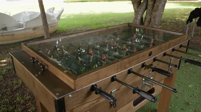 Wooden foosball table with glass top set outdoors on grass under trees