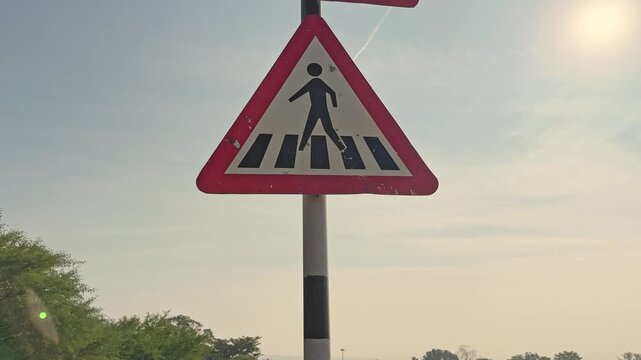 Tilt-up video shot showing a T-intersection ahead warning sign above a pedestrian crossing sign, alerting drivers to an upcoming road junction and zebra crossing on a highway in India.
