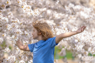 Free spring. Peaceful kid with raised hands meditating, feeling calm near cherry blossom tree. Kid practice yoga and relaxed on spring nature. Kid closed eyes and feeds energy of nature, dreams.