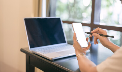 Mock up smart phone white background over shoulder blur laptop computer background, Social media mobile application concept in women hand well space for montage presentation.