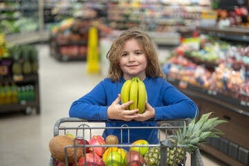 Fototapeta premium Children picking fresh fruits in the supermarket. Healthy vegetables in a kids shopping cart. Kid groceries at the market. Kid in a supermarket. Child shopping vegetables. Grocery shopping with kids.
