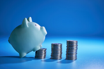 piggy bank and few stack of coins on blue background