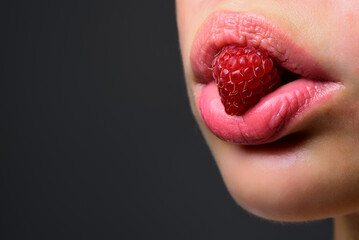 Close up of tongue holding a fresh raspberry. Creative macro concept with berry in mouth. Beauty on...