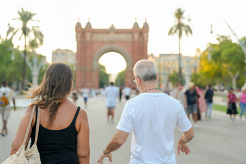 A man and woman are walking in a crowded city street. The man is wearing a white shirt and the woman is wearing a black tank top. They are both holding handbags. The scene is lively