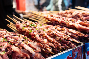 Traditional Dongguan street food: grilled octopus tentacles on a barbecue grill, at a street food market in Dongguan City, Guangdong Province, China. © chuangxin