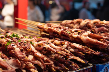 Traditional Dongguan street food: grilled octopus tentacles on a barbecue grill, at a street food market in Dongguan City, Guangdong Province, China. © chuangxin
