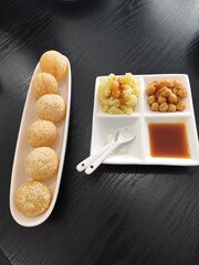 Pani puri is served on a white ceramic plate with side dishes of mashed potatoes, chickpeas, and sweet sauce.