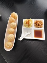 Pani puri is served on a white ceramic plate with side dishes of mashed potatoes, chickpeas, and sweet sauce.
