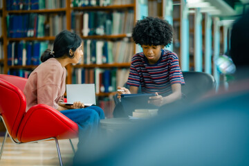 Students sitting together in library lounge discussing study notes using tablet showing collaborative learning academic focus self learning routine modern education environment.