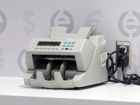 Calgary, Alberta, Canada. Dec 29, 2025. Professional Cummins Allison JetCount Currency Counter Machine on a White Table. A grey desktop bill counter plugged into a wall, featuring a digital display.
