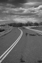 A winding levee road curves under a dramatic winter sky in monochrome