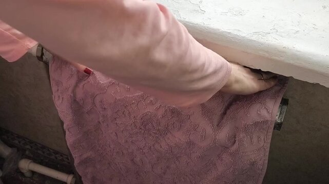 A woman hangs a towel on an old heating radiator. High temperature, heat in the house. Dry indoor air. Old Battery