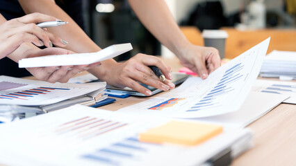 Professional business team analyzing financial growth charts and data on digital tablet and paperwork during a strategic meeting in a modern bright office space.