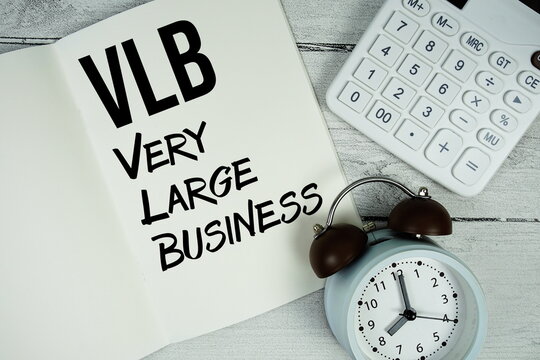 VLB Very Large Business text on paper notebook page with alarm clock and calculator on wooden background