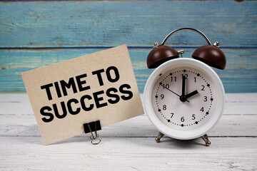 Time To Success text written on paper card with alarm clock on wooden background