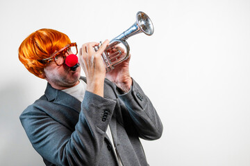 Clown playing trumpet with red nose and wig