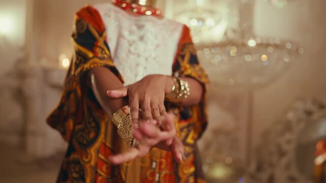 Black woman in ethnic african gown demonstrating golden jewelry on hands. Beautiful young lady dancing and showing her bracelets, traditional arabic dance show, closeup view of female arms and body