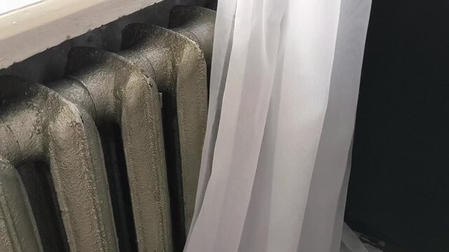 The curtains open and the old heating radiator becomes visible. Heating in the house with old radiators