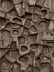 Industrial decay defines this sepia-toned wall of interlocking concrete forms and weathered circular depressions.