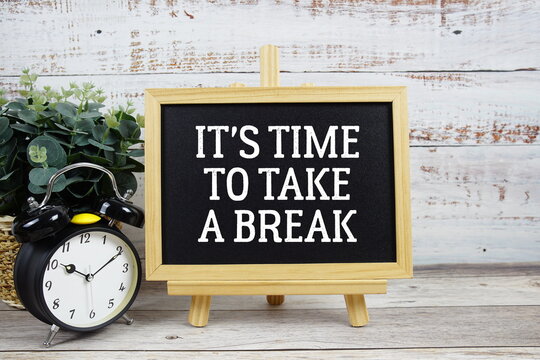 It's time to take a break text written on blackboard with alarm clock on wooden background