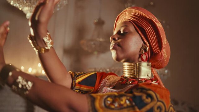 Luxury gold bracelets on hands of beautiful african female dancer, dance show. Medium portrait of attractive black lady in traditional african arabic gown performing dance in studio, rich and wealth