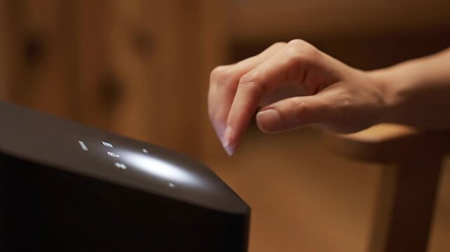 Close-up of woman's hand using black modern wireless speaker with touch controls.  Music, technology, audio.