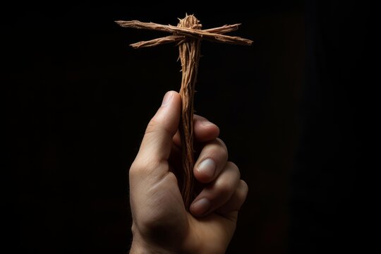 Hand holding a spiritual wooden cross against a deep black background