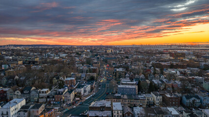 Aerial view of Jersey City skyline at sunset with Manhattan glowing across the Hudson River under dramatic evening clouds and warm city light creating a cinematic urban travel scene