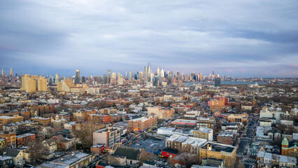 Aerial sunset panorama of Jersey City with Manhattan skyline in the distance showcasing dense urban neighborhoods glowing beneath colorful winter evening skies