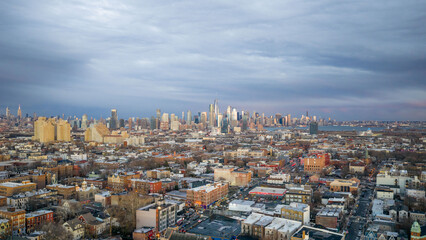 Wide aerial sunset view over Jersey City urban landscape featuring residential blocks and distant Manhattan skyline framed by calm winter evening sky