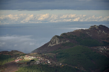 Mountain landscape forested hills slopes small village with houses and red roofs rocky peaks clouds...