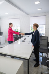Caucasian man and woman greeting and shaking hands in office. 