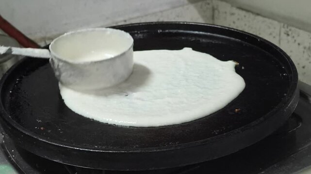 Video clip showing dosa batter being poured onto a hot tawa during cooking, highlighting South Indian cuisine, traditional breakfast preparation, and authentic Indian food-making process.
