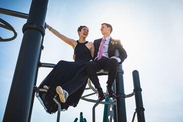 Teen couple in formal clothing smile atop a playground structure © Cavan