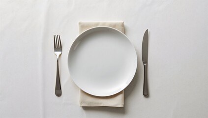 Simple overhead view of a single empty white dinner plate set with polished silver fork and knife resting on a beige linen napkin above a clean white tablecloth.