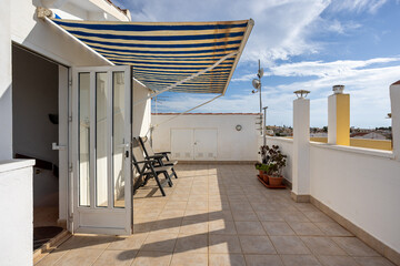 Spacious rooftop terrace with striped awning, outdoor chairs, and cityscape view