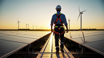 Engineer walking through solar panel farm at sunset with wind turbines in background, 4k high quality - Powered by Adobe
