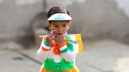 Candid portrait of a cute 2 year old Indian toddler girl holding the national flag stick near her...