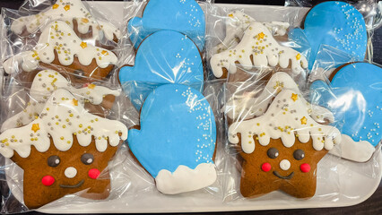Close-up of decorated gingerbread cookies in the shape of blue mittens and smiling stars in transparent packaging.