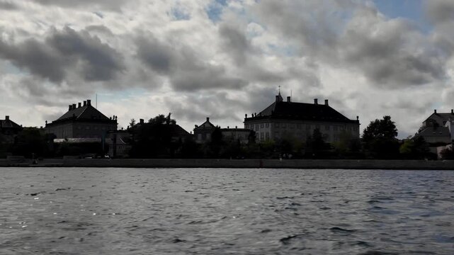 Cinematic establishing shot from a harbor boat passing the classical waterfront facade of Amalienborg Palace, the historic royal residence in Copenhagen, Denmark.