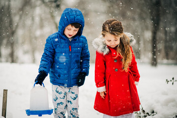 Children bringing bird feeder outdoors in winter snow