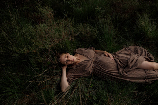 Pregant woman resting in tall grass wearing a brown dress