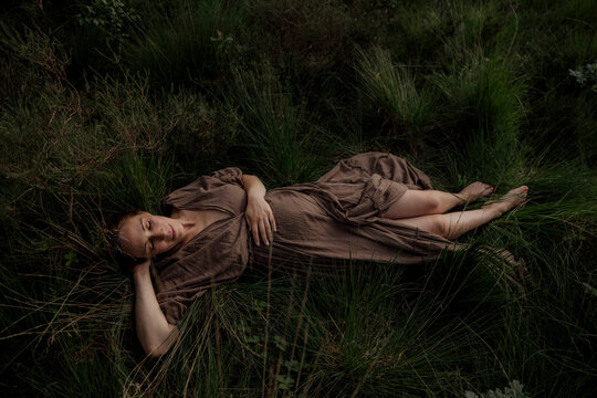 Pregant woman resting in tall grass wearing a brown dress