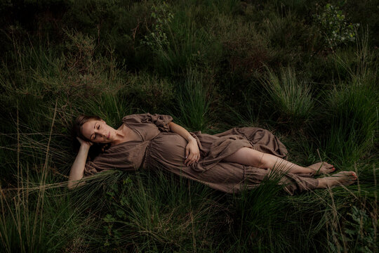 Pregant woman resting in tall grass wearing a brown dress
