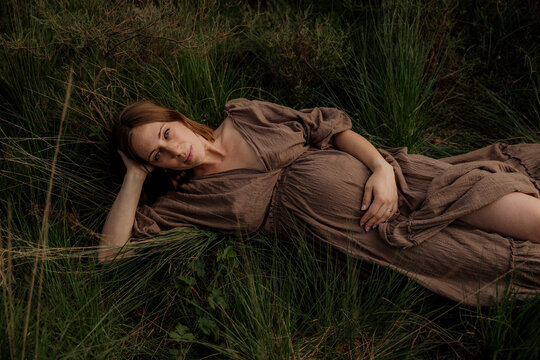 Pregant woman resting in tall grass wearing a brown dress