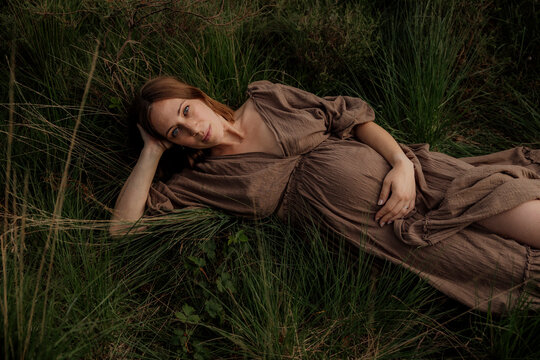Pregant woman resting in tall grass wearing a brown dress