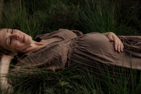 Pregant woman resting in tall grass wearing a brown dress