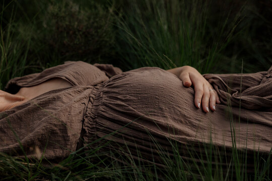 Pregant woman resting in tall grass wearing a brown dress